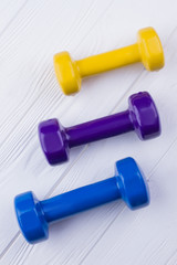 Colorful dumbbells on white wooden background. Top view on fitness equipment. Sport and healthy lifestyle.