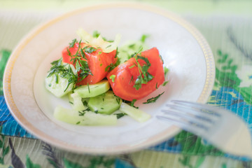 salad with fresh tomato, cucumber, pepper and greens on a white saucer with a fork.