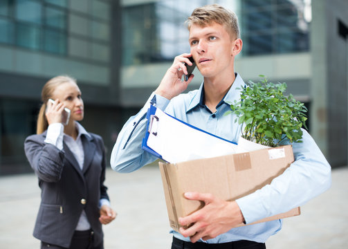 Young businessman with box is talking phone and searching new job
