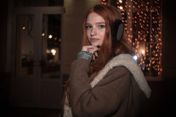 The portrait of an young redhear lady on the evening wearing earmuffs