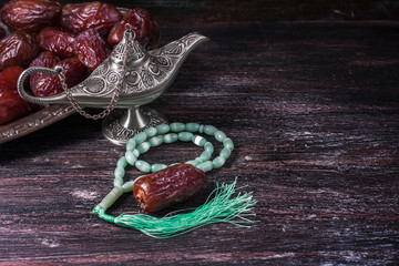 Fototapeta premium Green islamic prayer beads, dates and silver aladdin's lamp on a dark wooden background. Ramadan concept.