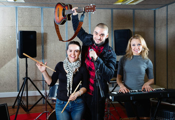 Three bandmates posing together with musical instruments in rehearsal room