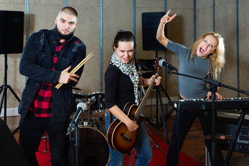 Fototapeta na wymiar Three bandmates posing together with musical instruments in rehearsal room