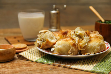Traditional Bosnian pastry- manti borek with meat on wooden table with yogurt. rustic background with low light and old bowls.