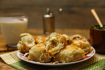 Traditional Bosnian pastry- manti borek with meat on wooden table with yogurt. rustic background with low light and old bowls.