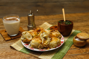Traditional Bosnian pastry- manti borek with meat on wooden table with yogurt. rustic background with low light and old bowls.