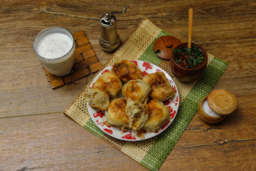 Traditional Bosnian pastry- manti borek with meat on wooden table with yogurt. rustic background with low light and old bowls.