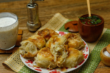 Traditional Bosnian pastry- manti borek with meat on wooden table with yogurt. rustic background with low light and old bowls.