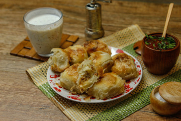 Traditional Bosnian pastry- manti borek with meat on wooden table with yogurt. rustic background with low light and old bowls.