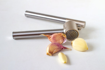 Metal garlic press and garlic cloves on light surface