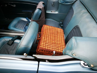 Picknickkoffer aus braunem Korbgeflecht auf dem Rücksitz eines amerikanischen Cabriolet mit blauem...