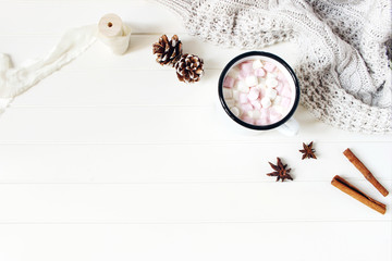 Christmas styled composition. Hot chocolate, marshmallow,cinnamon sticks, anise stars, pine cones and knitted blanket on white wooden table background. Winter breakfast concept. Flat lay, top view.