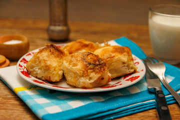 Traditional Bosnian pastry- manti borek with cheese on wooden table with yogurt. rustic background with low light and old bowls.