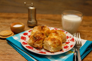 Traditional Bosnian pastry- manti borek with cheese on wooden table with yogurt. rustic background with low light and old bowls.