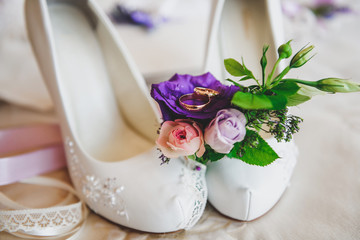 Gold wedding rings lie on the bride's shoes.
