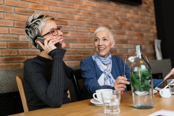 Senior mother sitting in cafe bar or restaurant with her middle age daughter and enjoying in conversation.