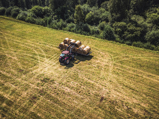 Obraz premium Aerial Drone Photo of Farmer Harvesting Hay Rolls in the Wheat Field with a Red Tractor