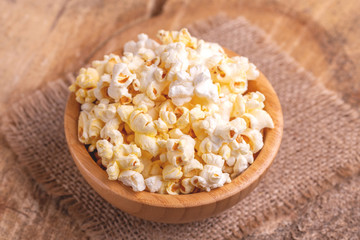 Tasty salty popcorn in wooden bowl on burlap napkin