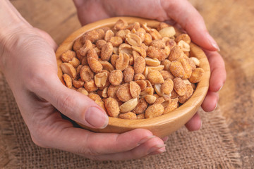 Wooden bow of roasted peanuts in womans hands