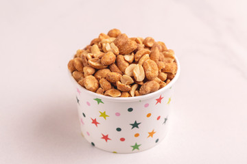 Roasted peanuts in paper cup on light marble background