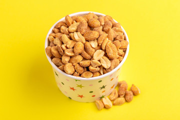 Roasted peanuts in paper cup on bright yellow background.
