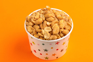 Roasted peanuts in paper cup on bright orange background