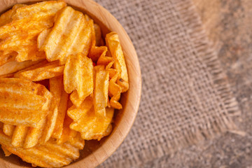 Crispy corrugated potato chips in wooden bowl on burlap napkin