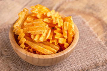 Crispy corrugated potato chips in wooden bowl on burlap napkin