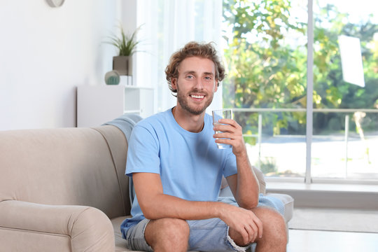 Young man holding glass of clean water indoors