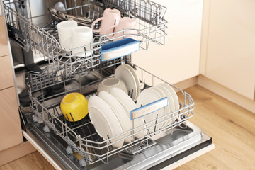 Open dishwasher with clean tableware in kitchen