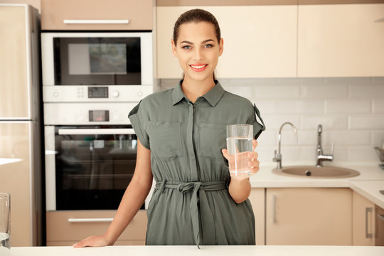 Young woman holding glass with water in kitchen