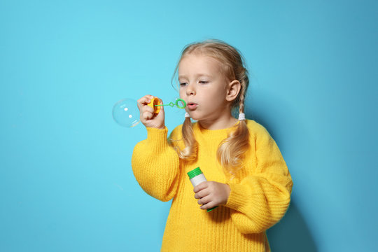 Cute little girl blowing soap bubbles on color background. Space for text