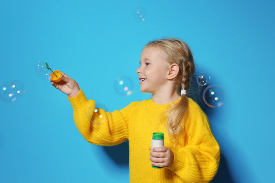 Cute little girl blowing soap bubbles on color background