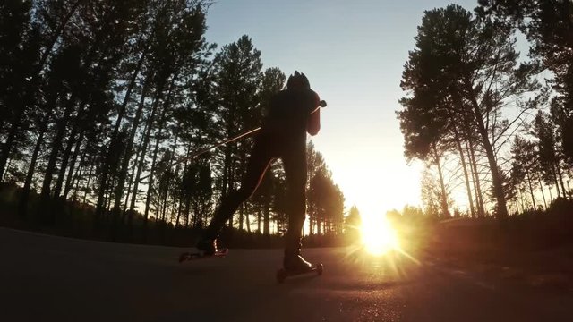 Training an athlete on the roller skaters. Biathlon ride on the roller skis with ski poles, in the helmet. Autumn workout. Roller sport. Adult man riding on skates. Shooting action cam. Slow motion.