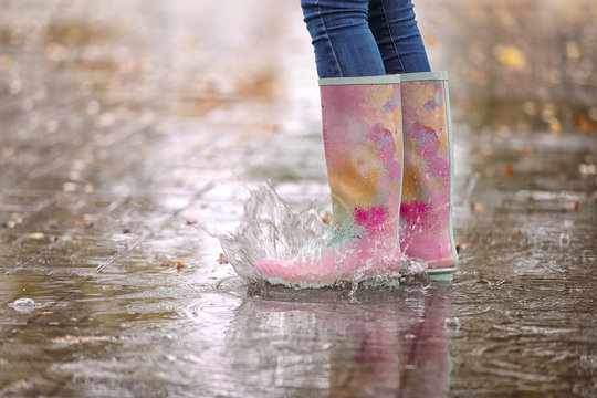 Woman wearing rubber boots splashing in puddle after rain, focus on legs. Autumn walk