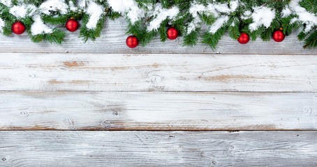 Snowy Christmas evergreen branches and red ornaments on white vintage wooden planks