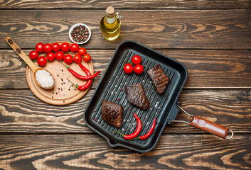 steaks, roast beef in a frying pan with spices, tomatoes, chili pepper, on wooden background, top view, beside chopped beef on a board