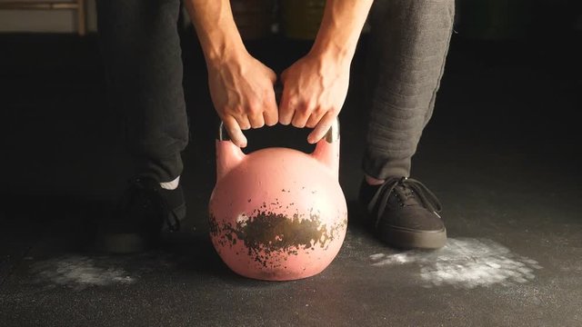 Slo-mo shot. Closeup of man's hands lifting pink kettlebell.