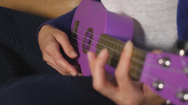Detail of caucasian woman's hand playing purple ukelele. Strumming hand and thumb in focus.