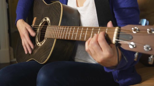 Caucasian woman strums acoustic guitar. Focus on strumming hand.