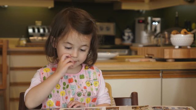 3 year old girl at the kitchen table flips through picture book.