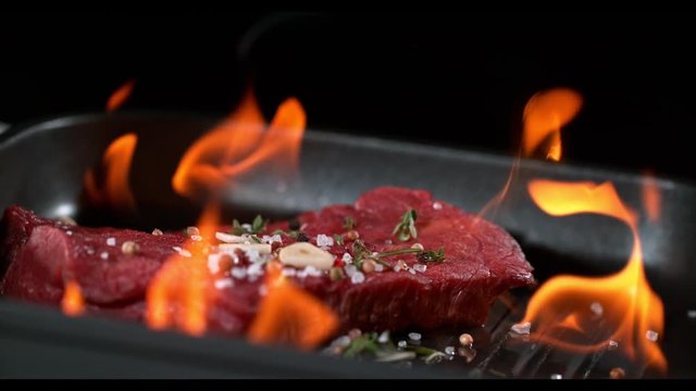 Super slowmotion footage of flambe fresh beef meat and seasoning on ignited pan, 1000fps 4k