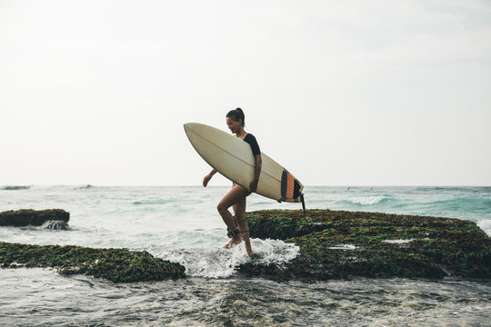 Woman surfer with surfboard walking on mossy seashore