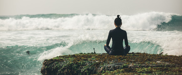 Yoga woman meditation at the seaside cliff edge facing the coming strong sea waves