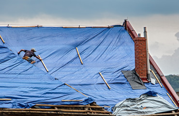 The roofer works on roof when is rain. The tarp covers the roof of the old house in the...