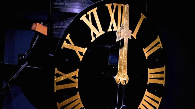 The clock with gilded Roman numerals shows exactly twelve hours. A bells on clock tower beat accurately the midnight. Clock mechanism with the bells.