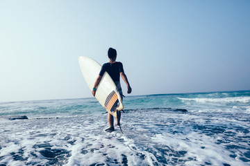 Woman surfer with surfboard walking on mossy seashore reefs