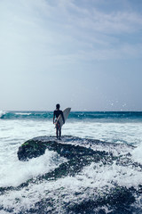Woman surfer with surfboard on mossy seashore reefs