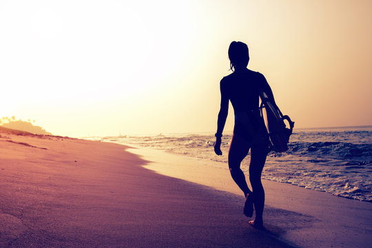 Surfer woman with surfboard walking on tropical beach