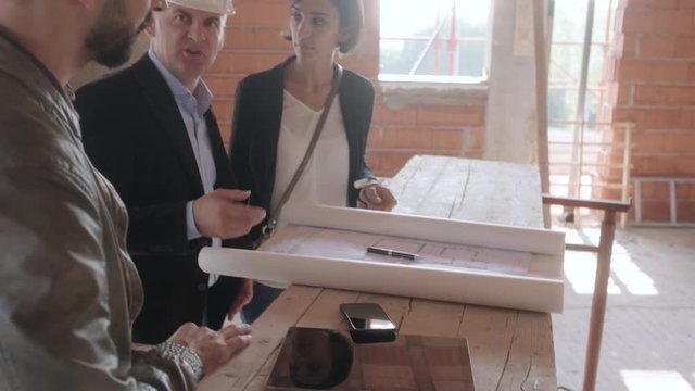 Sales agent talking with clients in new building. Man working as realtor in construction site with customers. Real estate broker showing home to husband and wife. Young couple as buyers of new house